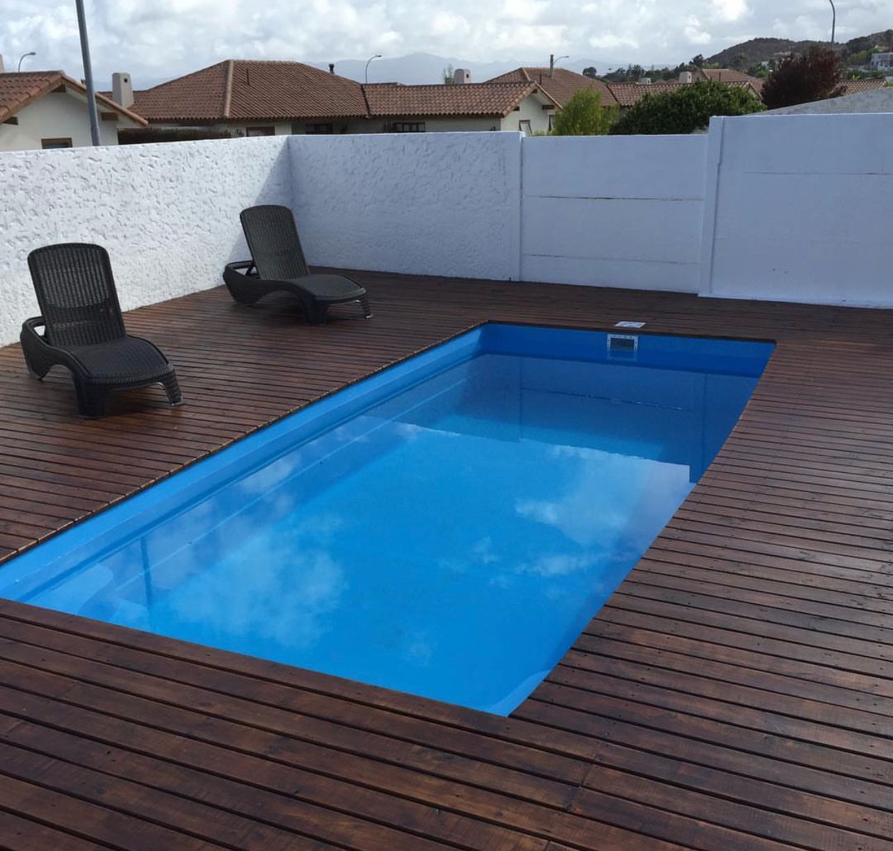 Piscina rectangular con deck de madera y postes rústicos, vista al mar